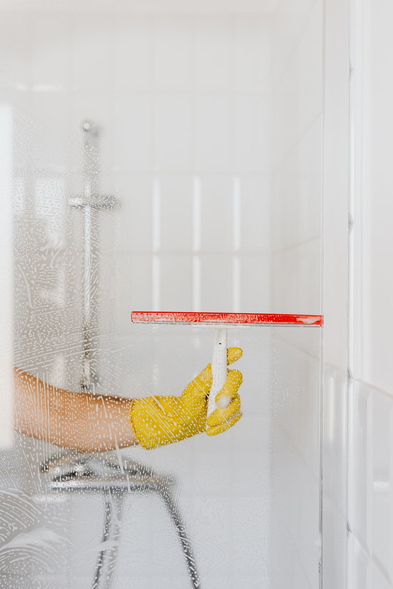 Hand cleaning a glass shower door in a bright residential bathroom. Stock photograph; not a SpenceCo project.